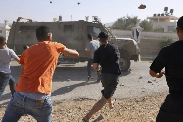 Palestinian youths throw rocks at an Israeli army jeeps in the town of Silwad, near the city of Ramallah in the occupied West Bank, after a military operation in the town, on August 31, 2022. (Photo by Abbas Momani/AFP Photo)