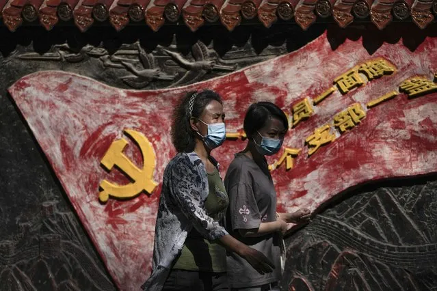 Women wearing face masks walk by a mural depicting a communist party flag and a party slogan in Beijing, Tuesday, September 6, 2022. China has locked down millions of its citizens under tough COVID-19 restrictions and is discouraging domestic travel during upcoming national holidays. (Photo by Andy Wong/AP Photo)