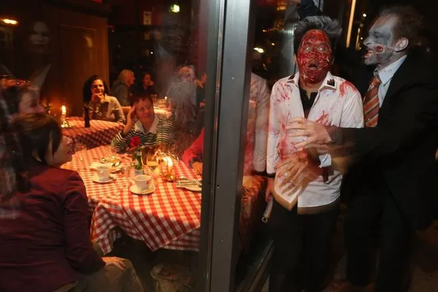 Diners in a restaurant look on as zombie enthusiasts walk by during a “Zombie Walk” in the city center on October 27, 2012 in Berlin, Germany. Approximately 150 zombies, who had organized themselves through Facebook, walked and limped across Alexanderplatz, growled and moaned at passersby and performed jerking dances. (Photo by Sean Gallup)