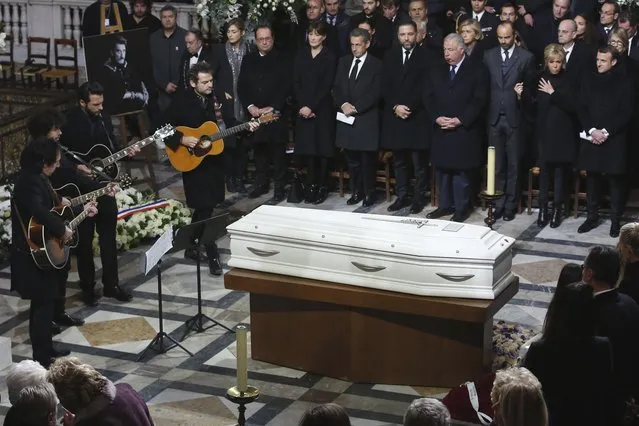 French musician Matthieu Chedid (R) plays guitar next to the coffin during the funeral ceremony of late French singer Johnny Hallyday next to (back-L) French actress Julie Gayet, former French President Francois Hollande, Carla Bruni, former French President Nicolas Sarkozy, an unidentified official, French Senate President Gerard Larcher, French Prime Minister Edouard Philippe, Brigitte Macron and French President Emmanuel Macron  at the Eglise de la Madeleine (La Madeleine Church) in Paris, on December 9, 2017. French music icon Johnny Hallyday died on December 6, 2017 aged 74 after a battle with lung cancer, plunging the country into mourning for a national treasure whose soft rock lit up the lives of three generations. (Photo by Thibault Camus/AFP Photo)