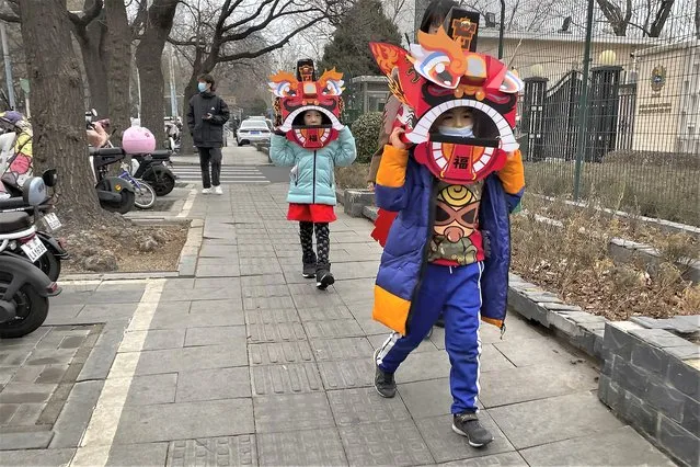 Children wearing cardboard lion dance masks walk along a street in Beijing on January 13, 2023. China has announced its first overall population decline in recent years amid an aging society and plunging birthrate. (Photo by Mark Schiefelbein/AP Photo)