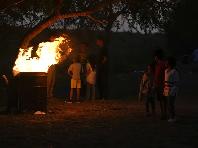 Venezuelan migrants huddle near an oil drum bonfire for warmth at a makeshift camp along a river bank in Matamoros, Mexico, Thursday, December 22, 2022. (Photo by Fernando Llano/AP Photo)