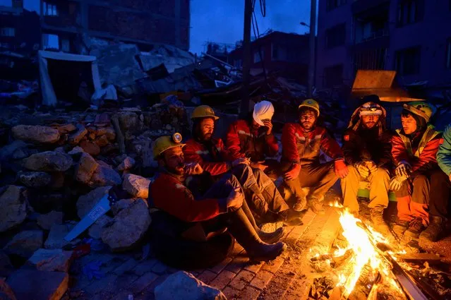 Rescuers sit by a bonfire in Hatay, on February 12, 2023, after a 7.8-magnitude earthquake struck the country's south-east. The death toll from a massive earthquake that hit Turkey and Syria climbed to more than 20,000 on February 9, 2023, as hopes faded of finding survivors stuck under rubble in freezing weather. (Photo by Yasin Akgul/AFP Photo)