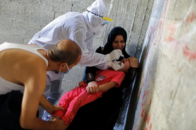 A healthcare worker in protective gear collects a swab sample from a girl to be tested for the coronavirus disease (COVID-19), on the staircase of her family's home in Gaza City on September 21, 2020. (Photo by Suhaib Salem/Reuters)