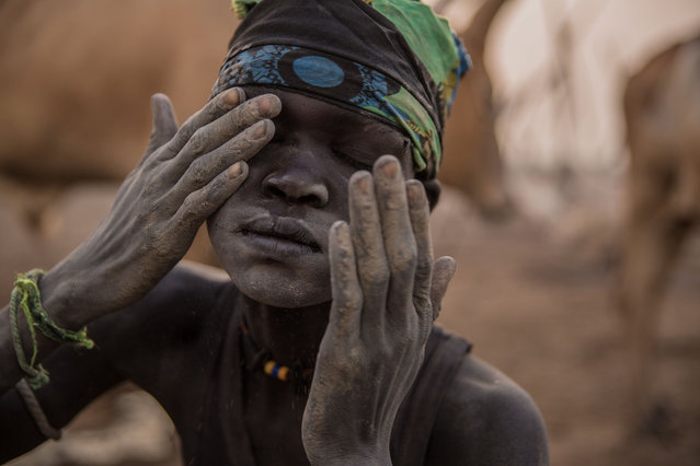 A Sudanese boy from Dinka tribe covers his face with an ash as mosquito repellent in the early morning at their cattle camp in Mingkaman, Lakes State, South Sudan on March 4, 2018. (Photo by  Stefanie Glinski/AFP Photo)