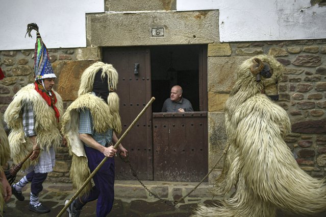 A resident looks at a group of Joaldunaks taking part in the traditional carnival between the Pyrenees villages of Ituren and Zubieta, Spain on January 31, 2022. The carnival has been cancelled due to Covid-19 for the last two years. This year it has returned as one of the most ancient carnival celebrations in Europe, with dozens of people donning sheepskins, lace petticoats, conical caps and cowbells as they parade to herald the advent of spring. (Photo by Alvaro Barrientos/AP Photo)