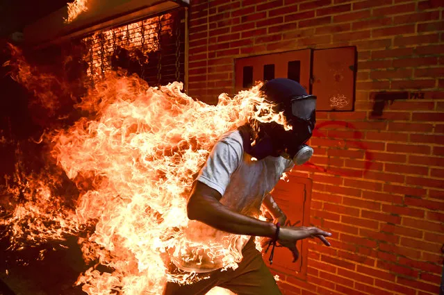 Venezuela crisis: José Víctor Salazar Balza (28) catches fire amid violent clashes with riot police during a protest against President Nicolás Maduro, in Caracas, Venezuela, May 3, 2017. President Maduro had announced plans to revise Venezuela’s democratic system by forming a constituent assembly to replace the opposition-led National Assembly, in effect consolidating legislative powers for himself. Opposition leaders called for mass protests to demand early presidential elections. Clashes between protesters and the Venezuelan national guard broke out on 3 May, with protesters (many of whom wore hoods, masks or gas masks) lighting fires and hurling stones. Salazar was set alight when the gas tank of a motorbike exploded. He survived the incident with first- and second-degree burns. (Photo by Ronaldo Schemidt/AFP Photo/World Press Photo)