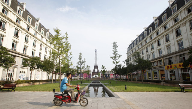 A man rides a motorcycle past a replica of the Eiffel Tower at the Tianducheng development in Hangzhou, Zhejiang Province August 1, 2013. Tianducheng, developed by Zhejiang Guangsha Co. Ltd., started construction in 2007 and was known as a knockoff of Paris with a scaled replica of the Eiffel Tower standing at 108 metres (354 ft) and Parisian houses. Although designed to accommodate at least 10 thousand people, Tianducheng remains sparsely populated and is now considered as a “ghost town”, according to local media. (Photo by Aly Song/Reuters)