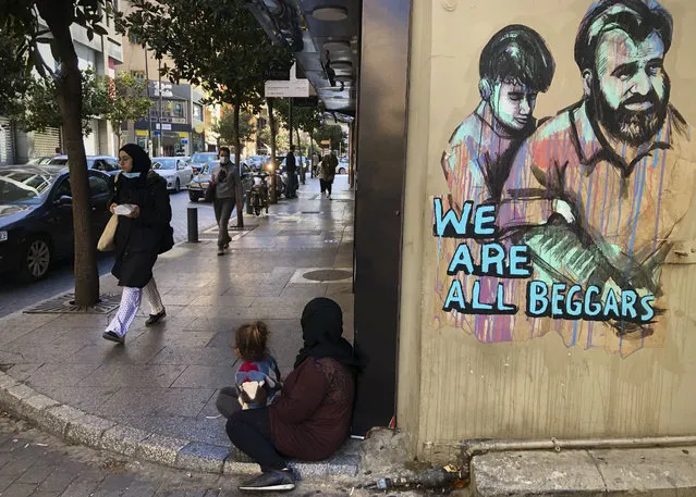 People pass next of a woman, center, who is sits on the ground with her daughter begging on Beirut's commercial Hamra Street, in Beirut, Lebanon, Tuesday, March 16, 2021. (Photo by Hussein Malla/AP Photo)