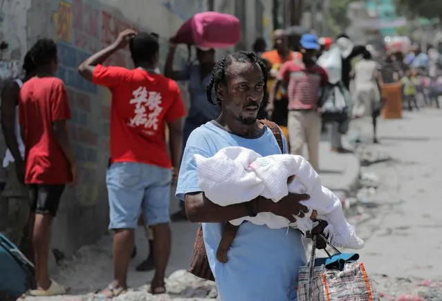 A man carries a baby as he and others flee their neighbourhood Carrefour Feuilles after gangs took over, in Port-au-Prince, Haiti on August 15, 2023. (Photo by Ralph Tedy Erol/Reuters)