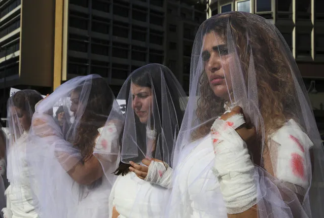 A dozen Lebanese women, dressed as brides in white wedding dresses stained with fake blood and bandaging their eyes, knees and hands stand in front of the government building in downtown Beirut, Lebanon, Tuesday, December 6, 2016. The activists are protesting a Lebanese law that allows a rapist to get away with his crime if he marries the survivor. The law, in place since the late 1940s, is currently reviewed in Lebanese parliament. Campaigners against the law are calling on lawmakers to repeal the law during their meeting Wednesday. (Photo by Bilal Hussein/AP Photo)