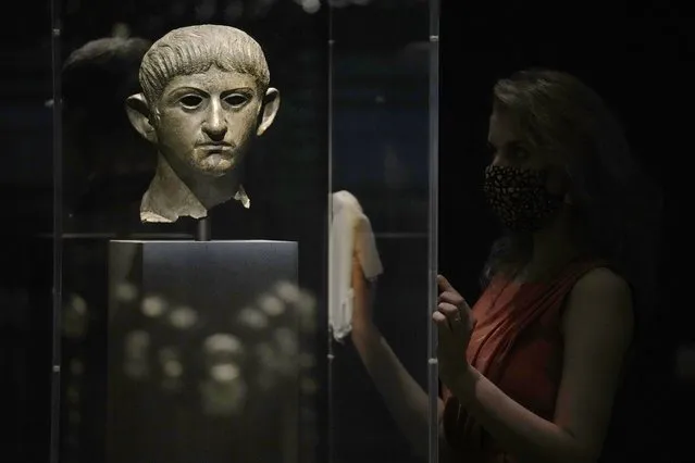 A museum employee poses for photographers next to a bronze head of Roman emperor Nero dating from around AD 54-61 and found in the River Alde at Rendham in Suffolk, eastern England, during a media preview for the “Nero: the man behind the myth” exhibition, at the British Museum in London, Monday, May 24, 2021. The exhibition, which opens to visitors on May 27 and runs until October 24, explores the true story of Rome's fifth emperor informed by new research and archaeological evidence from the time. (Photo by Matt Dunham/AP Photo)