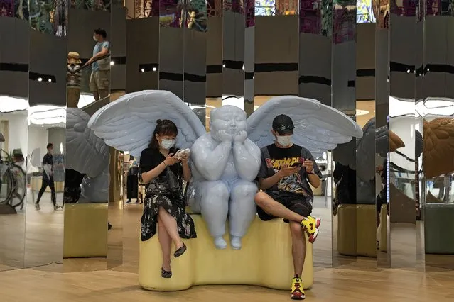 A couple wearing face masks to help curb the spread of the coronavirus sit on an angel statue browsing their smartphones at a shopping mall in Beijing, Sunday, June 6, 2021. (Photo by Andy Wong/AP Photo)