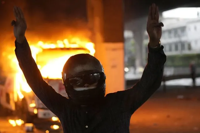 Anti-government protester display the three-finger symbol of resistance in front of burning police truck during protest in Bangkok, Thailand, Wednesday, August 11, 2021. (Photo by Sakchai Lalit/AP Photo)