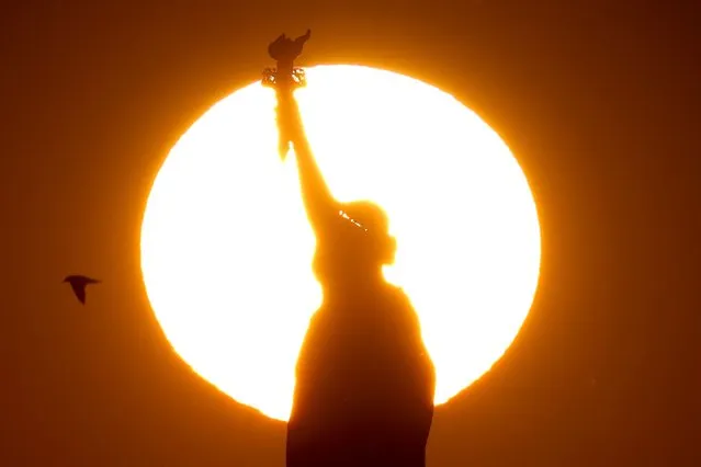 The sun sets behind the Statue of Liberty in New York City on December 13, 2023. (Photo by Charly Triballeau/AFP Photo)