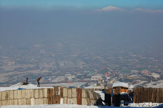 A man walks on the roof of a traditional ger home while fixing the chimney of a coal burning stove on a cold hazy day on the outskirts of Ulaanbaatar, Mongolia January 19, 2017. On most winter mornings, Setevdorj Myagmartsogt wakes up to a cloud of toxic smog blanketing his neighbourhood in the Mongolian capital Ulaanbaatar, where the air quality is among the worst in the world. The city's air, which is at times far worse than Beijing's infamous smog, has become more polluted because of smoke from thousands of chimneys burning coal, wood and even trash, as poor residents try to stay warm during brutal winters. (Photo by B. Rentsendorj/Reuters)