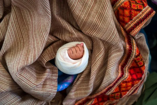 Hand of a baby juts out of the shawl of an exile Tibetan woman as she attends a short sermon delivered by Tibetan spiritual leader the Dalai Lama on the 15th day of the first Tibetan month at the Tsuglakhang temple in Dharamshala, India, Saturday, February 24, 2024. (Photo by Ashwini Bhatia/AP Photo)