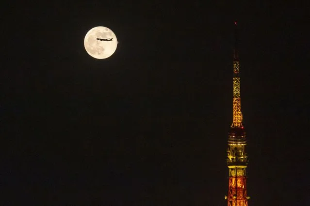 An airplane flies past the moon rising over Tokyo Tower Saturday, November 20, 2021, in Tokyo. (Photo by Kiichiro Sato/AP Photo)