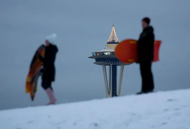 Visitors at the top of the Space Needle are seen as a couple pauses at the top of Kite Hill at Gas Works Park, a popular sledding location, after a recent snowfall in Seattle, Washington, U.S. December 27, 2021. (Photo by Lindsey Wasson/Reuters)