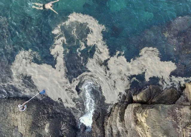This aerial photo shows a man (bottom L) cleaning tiny pumice stones from the sea at the Waimushan Seaside area in the city of Keelung on December 16, 2021, after the debris drifted to the northern coast of Taiwan from the Fukutoku-Okanoba underwater volcano which began erupting some 1,280 km (800 miles) off the southern coast of Japan in August. (Photo by Sam Yeh/AFP Photo)