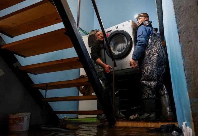Resident Dmitry Dragoshantsev is helped by a friend to carry a washing machine out of a flooded ground floor in his house in Orenburg, Russia, on April 12, 2024. (Photo by Maxim Shemetov/Reuters)