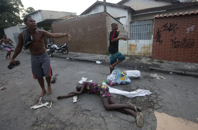 A woman affected by tear gas lies on the ground during an eviction in Rio de Janeiro, Brazil, Friday, April 11, 2014. Squatters in Rio de Janeiro are clashing with police after a Brazilian court ordered that 5,000 people be evicted from abandoned buildings of a telecommunications company. Officers have used tear gas and stun grenades to try to disperse the families. (Photo by Silvia Izquierdo/AP Photo)