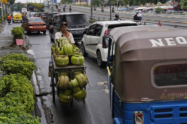 A worker transporting gas canisters pushes his cart against the traffic flow in Jakarta, Indonesia, Tuesday, January 25, 2022. (Photo by Dita Alangkara/AP Photo)