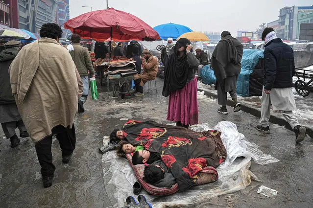 A woman shouts and begs for alms next to children sleeping on a market area on a cold day in Kabul on January 19, 2022. (Photo by Mohd Rasfan/AFP Photo)