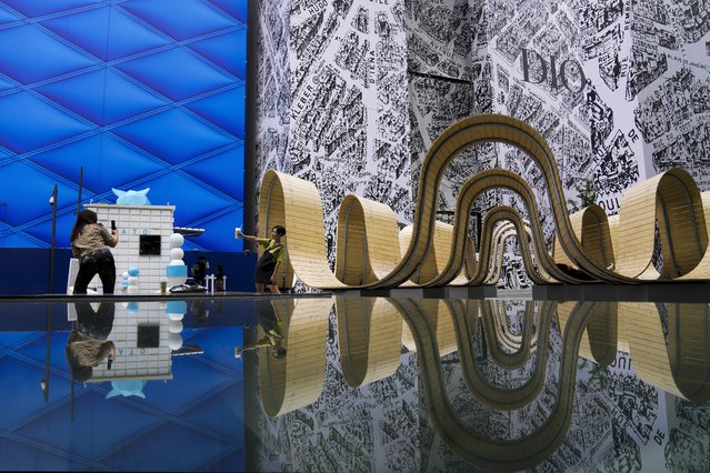 A woman holding a cup of coffee poses for a souvenir photo with an art installation reflected at an outdoor luxury shopping mall in Beijing, Wednesday, June 5, 2024. (Photo by Andy Wong/AP Photo)