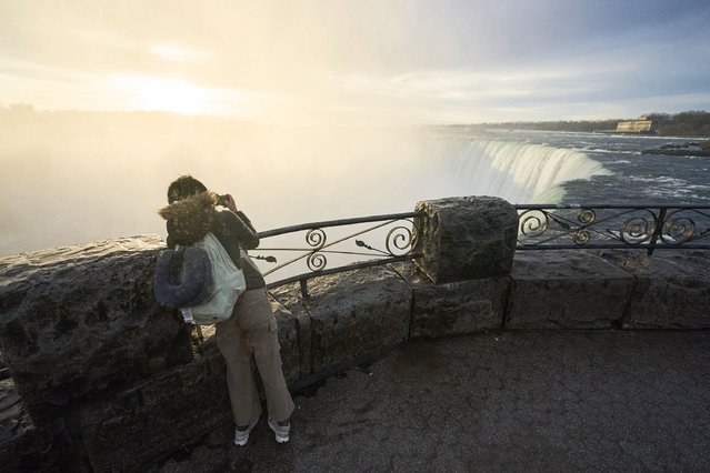 A person takes a photo as the sun rises over Horseshoe Falls in Niagara Falls, Ontario, Canada, on April 8, 2024 as they prepare for the total eclipse which is set to pass over the region later in the day. This year's path of totality is 115 miles (185 kilometers) wide and home to nearly 32 million Americans, with an additional 150 million living less than 200 miles from the strip. The next total solar eclipse that can be seen from a large part of North America won't come around until 2044. (Photo by Geoff Robins/AFP Photo)