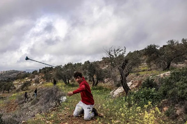 A Palestinian protester uses a slingshot to hurl a stone at Israeli security forces during clashes following a demonstration against settlements in the village of Beita in the occupied West Bank on February 25, 2022. (Photo by Ronaldo Schemidt/AFP Photo)