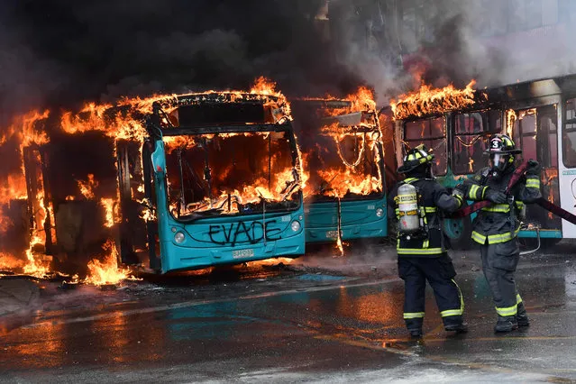 Chilean firefighters extinguish a burning bus during clashes between protesters and the riot police in Santiago, on October 19, 2019. Chile's president declared a state of emergency in Santiago Friday night and gave the military responsibility for security after a day of violent protests over an increase in the price of metro tickets. (Photo by Martin Bernetti/AFP Photo)