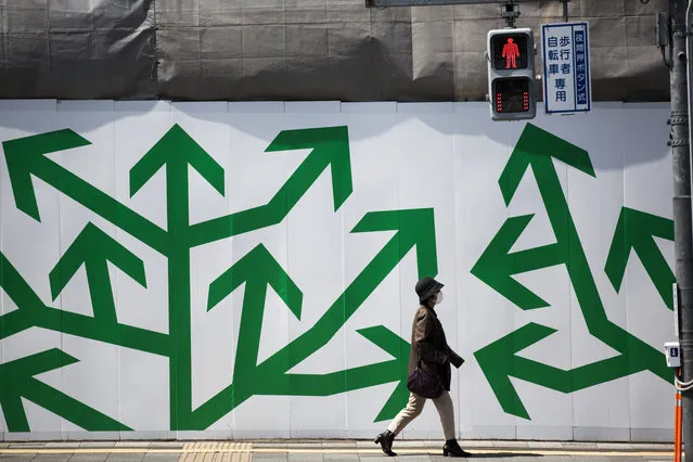 A pedestrian walks past decorated panelling used to shroud a construction site along a street in Tokyo on April 5, 2017. (Photo by Behrouz Mehri/AFP Photo)