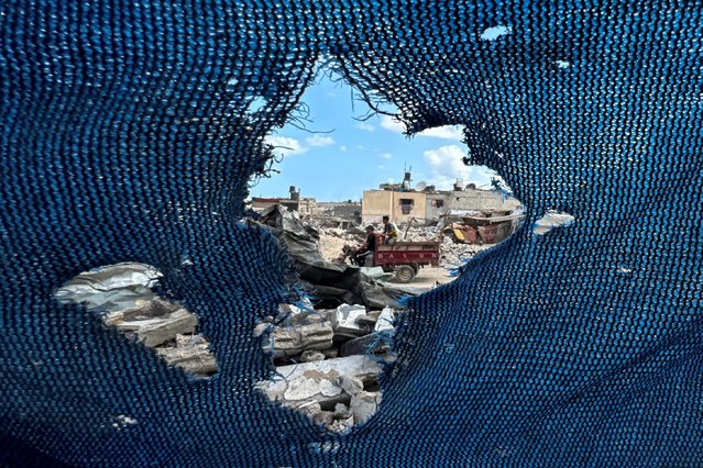 Palestinians, seen through a torn tent, ride a motorized vehicle past the rubble, amid the Israel-Hamas conflict, in Khan Younis, in the southern Gaza Strip on September 16, 2024. (Photo by Mohammed Salem/Reuters)