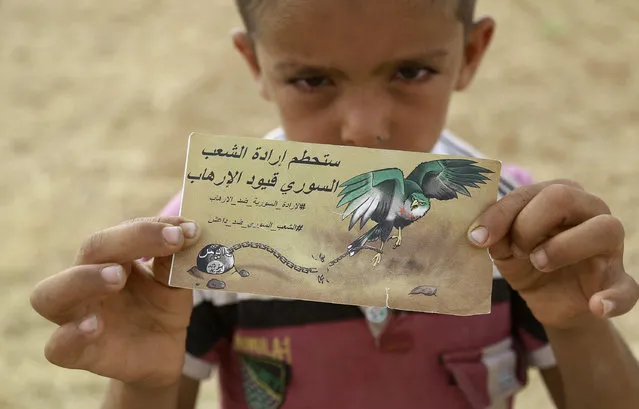 A young Syrian boy holds a banner dropped by a Syrian Democratic Forces (SDF) alliance plane reading in Arabic: “The will of the Syrian people will break the chains of the terrorists” as US-backed Kurdish and Arab fighters advance into the Islamic State (IS) jihadist's group bastion of Manbij, in northern Syria, on June 23, 2016. Backed by air strikes by the US-led coalition bombing IS in Syria and Iraq, fighters with the Syrian Democratic Forces (SDF) alliance entered Manbij from the south, a monitoring group said. (Photo by Delil Souleiman/AFP Photo)