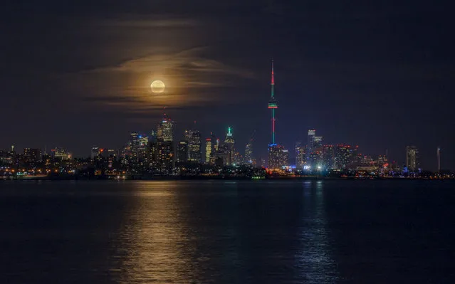 Christmas Full Moon Rise, Toronto, Canada. The thinning cloud layer seen across the face of the moon acted as a natural filter to reduce its brightness, offering the photographer a chance to try imaging the moonrise over the colourful skyline. The photographer had wondered whether it would be possible to photograph such a moonrise and finally decided to take the technical challenge with his eight-year-old camera and was fortunate enough to obtain a memorable image. (Photo by Andrew Yee/National Maritime Museum)
