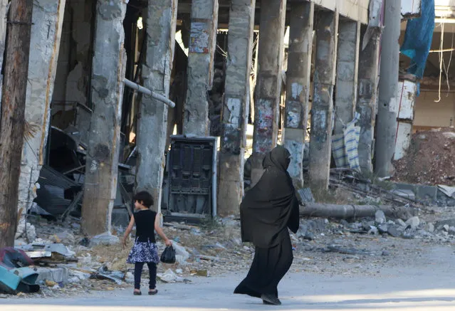 Residents walk past damaged buildings in the rebel held area of Aleppo's Bab al-Hadeed district, Syria, June 27, 2016. (Photo by Abdalrhman Ismail/Reuters)