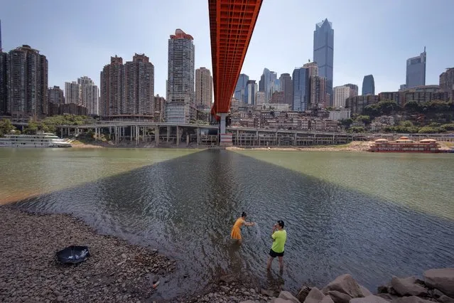 People look at a dead fish on the dried-up riverbed of the Jialing river, a tributary of the Yangtze, that is approaching record-low water levels in Chongqing, China on August 18, 2022. (Photo by Thomas Peter/Reuters)