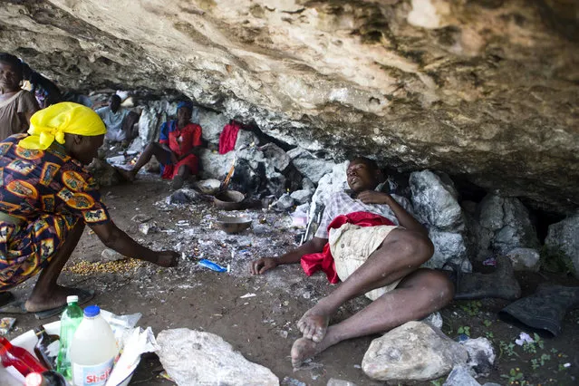 In this July 23, 2016 photo, a Voodoo pilgrim places a candle in a crevice next to a sleeping man in Plaine-du-Nord, Haiti. People pray and make offerings at Plaine-du-Nord's Catholic church of St. James, who is known as Ogoun Feraille and revered by followers of Voodoo. (Photo by Dieu Nalio Chery/AP Photo)