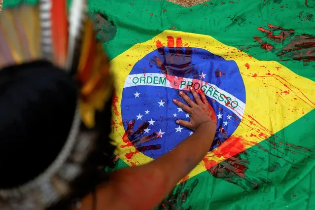 A Guarani indigenous woman covers a Brazilian flag in red paint during a protest marking International Indigenous Women's Day and Amazon Day, celebrated on September 5, and in defence of the Amazon and the Brazilian biomes, in Sao Paulo, Brazil September 4, 2022. (Photo by Amanda Perobelli/Reuters)