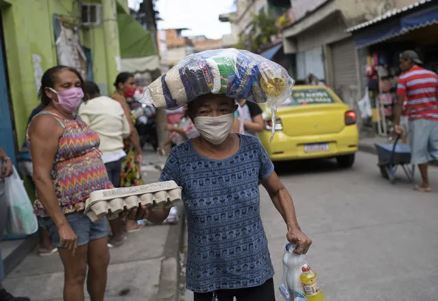 Maria Rita Dias dos Santos, 53, wearing a protective face mask, carries food donated food from former inmates, part of a nonprofit organization known as  “Eu sou Eu” or “I am me”, who are delivering food to people struggling due to the new coronavirus pandemic, at the Para-Pedro favela in Rio de Janeiro, Brazil, Friday, May 8, 2020. (Photo by Silvia Izquierdo/AP Photo)