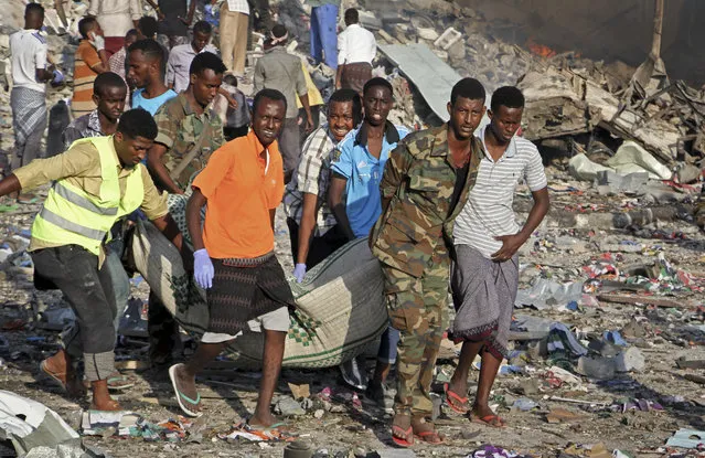 Somalis remove the body of a man killed in a blast in the capital Mogadishu, Somalia Saturday, October 14, 2017. A huge explosion from a truck bomb has killed at least 20 people in Somalia's capital, police said Saturday, as shaken residents called it the most powerful blast they'd heard in years. (Photo by Farah Abdi Warsameh/AP Photo)