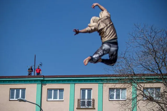 People look out from roof to a member of the contemporary circus company Cirk La Putyka performing on the mobile trampoline as he amuses local residents in Prague, Czech Republic, 09 April 2020. The aim of the Cirk La Putyka events in the streets of Czech capital is to get live art back to people during the lockdown. According to them, when people can't go to the artists, to the theater, the actors go to the people. The Czech government has imposed a lockdown in an attempt to slow down the spread of the pandemic COVID-19 disease caused by the SARS-CoV-2 coronavirus. (Photo by Martin Divisek/EPA/EFE)