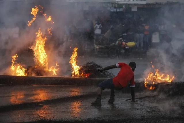 A supporter of the opposition coalition the National Super Alliance (NASA) and its presidential candidate Raila Odinga gets up after slipping and falling in the rain in front of a burning barricade he and others set up to block vehicles from delivering electoral materials to the polling stations in ther areas in Kibera slum, one of the opposition strongholds in Nairobi, Kenya, October 25, 2017. (Photo by Dai Kurokawa/EPA/EFE)