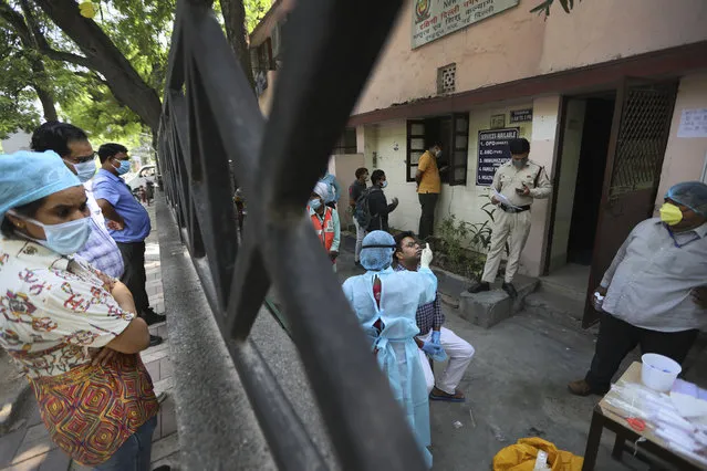 In this Wednesday, June 10, 2020 photo, people look on as health workers take swab test for COVID 19 in New Delhi, India. Two and a half months of nationwide lockdown kept numbers of infections relatively low in India. But with restrictions easing in recent weeks, cases have shot up, raising questions about whether authorities have done enough to avert catastrophe. Half of Delhi’s 8,200 hospital beds dedicated to COVID-19 patients are already full and officials are projecting more than half a million cases in the city alone by July 31. (Photo by Manish Swarup/AP Photo)