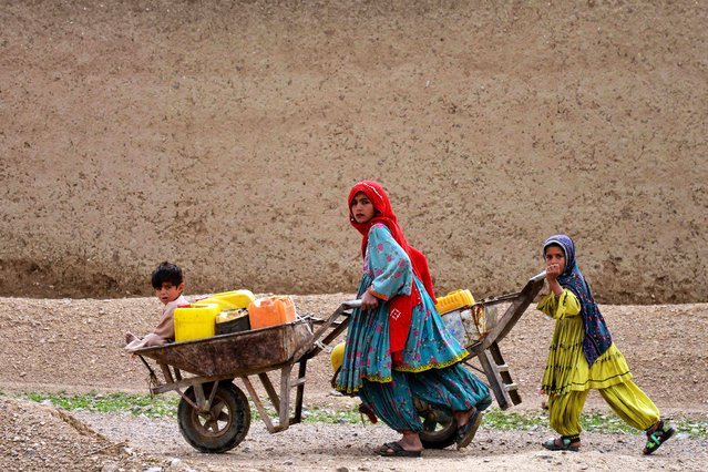 Afghan Kochi nomad girls push wheelbarrows as they fetch water along a street in Daman district of Kandahar province on February 26, 2025. (Photo by Sanaullah Seiam/AFP Photo)