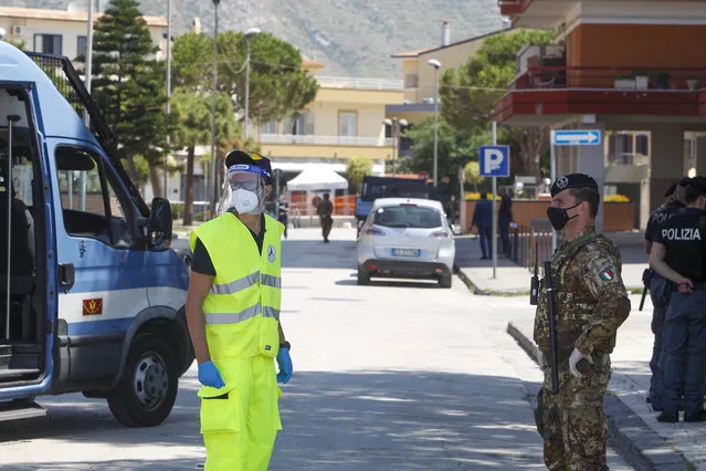 Civil protection and army officers stand at a road block in front of an apartment complex where dozens of COVID-19 cases have been registered among a community of Bulgarian farm workers, in Mondragone, in the southern Italian region of Campania, Friday, June 26, 2020. The governor of the region is insisting that the farm workers should stay inside for 15 days, not even emerging for food, and that the national civil protection agency should deliver them groceries. (Photo by Riccardo De Luca/AP Photo)