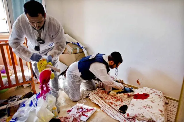 Zaka volunteers clean blood stains from a pillow and a baby toy in a children's room in an apartment building in Kiryat Malachi. (Photo by Ariel Schalit/Associated Press)