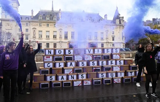 Demonstrators hold purple flare as they stand next to a wall made up of boxes of files, to symbolize the files closed without follow-up, with the inscription “our lives closed without follow-up” during a rally by the feminist collective NousToutes to protest against the inaction of the justice system in matters of sеxist and sexual violence, in front of the Palais de Justice, the historical courthouse located in the Île de la Cite in Paris, on November 23, 2022. (Photo by Bertrand Guay/AFP Photo)