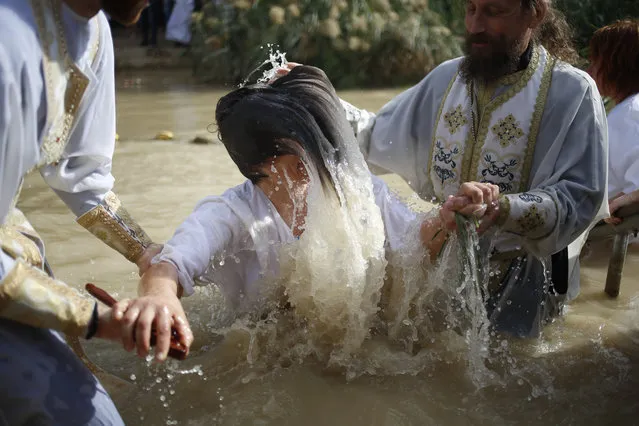 A Christian Orthodox priest re-enacts the baptism of Jesus, during the traditional Epiphany baptism ceremony at the Qasr-el Yahud baptism site in the Jordan river, near the West Bank town of Jericho, Thursday, January 18, 2018. (Photo by Ariel Schalit/AP Photo)